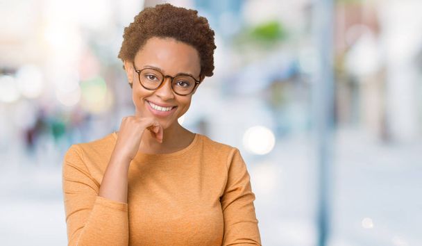 Mladá krásná africká americká žena nosí brýle izolované pozadí sebevědomým na kameru s úsměvem se zkříženýma rukama a ruku a na bradě. Pozitivní myšlení. - Fotografie, Obrázek