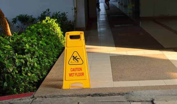 Közelkép kép a régi sárga figyelmeztető jel olvasható óvatosan nedves padlón, a sétányon, egy épületre  - Fotó, kép