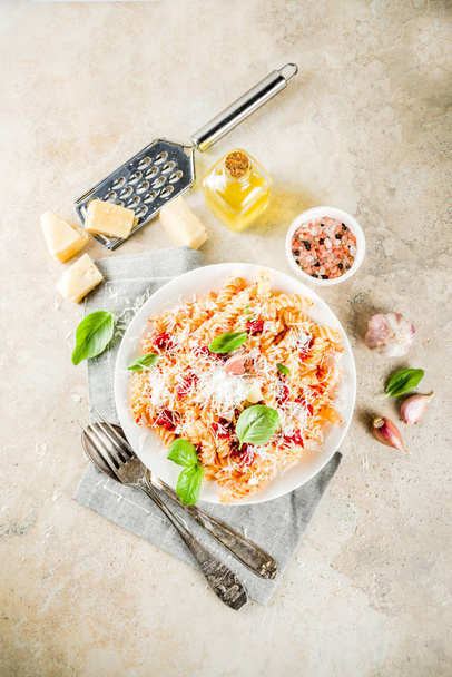 Włoskie jedzenie, fusilli makaron z sosem pomidorowym, tarty parmezan i bazylia, kamienny stół kopiować miejsca widok z góry - Zdjęcie, obraz