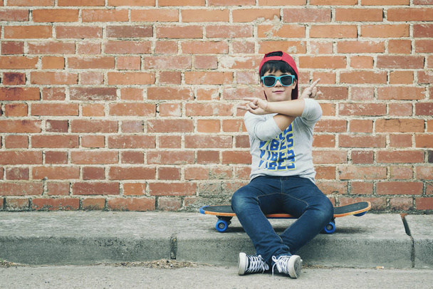 child with a skateboard and sunglasses in the street - Photo, Image