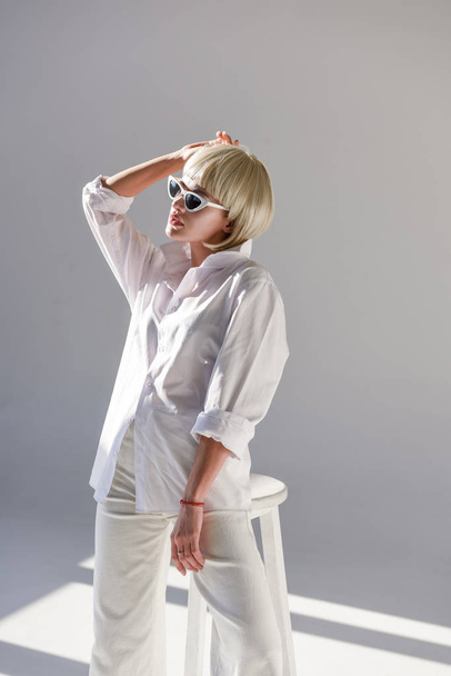 attractive blonde woman in sunglasses and fashionable white outfit on white - Foto, Imagen