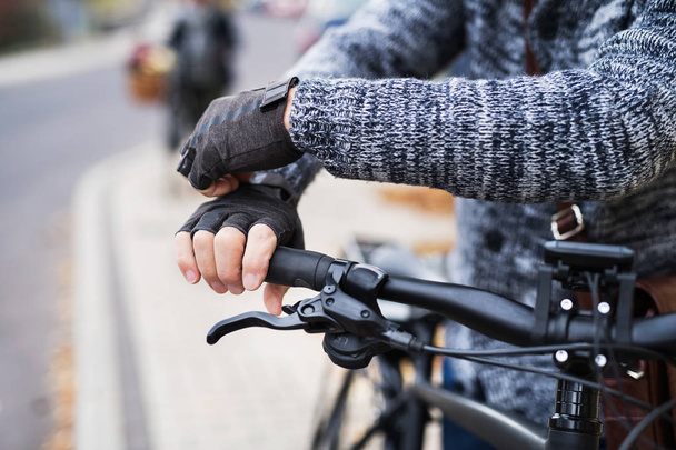 A close-up of a cyclist with electrobike putting on gloves outdoors in town. - Фото, изображение