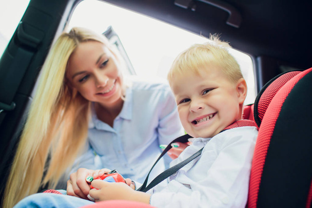 family, transport, road trip and people concept - happy woman fastening child with safety seat belt in car - Valokuva, kuva