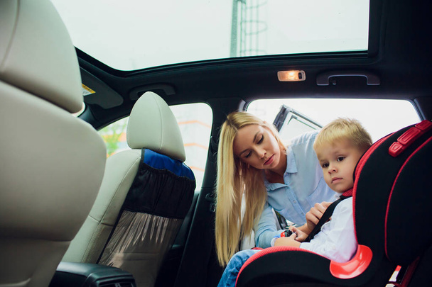 famille, transport, voyage sur la route et concept de personnes - femme heureuse attachant l'enfant avec la ceinture de sécurité dans la voiture
 - Photo, image