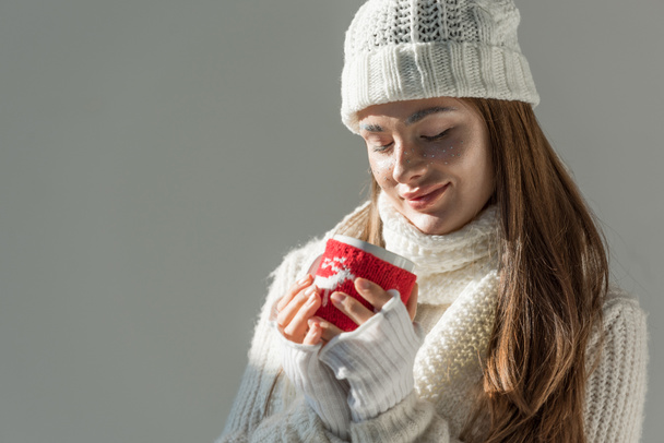 attractive woman in fashionable winter sweater and scarf holding cup of tea isolated on grey - Photo, Image