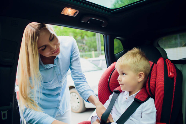 семья, транспорт, дорожная поездка и люди концепция - счастливая женщина пристегивая ребенка с ремнем безопасности в автомобиле
 - Фото, изображение