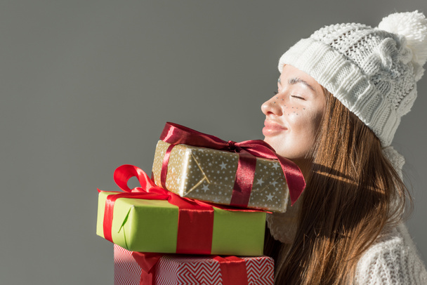 cheerful attractive woman in fashionable winter sweater and scarf holding gift boxes isolated on grey - Φωτογραφία, εικόνα