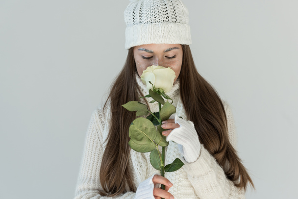 attractive woman in fashionable winter sweater and scarf sniffing white rose isolated on white - Фото, зображення