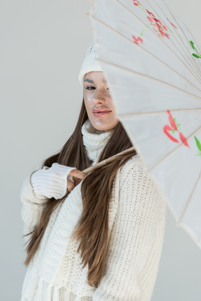 Porträt einer attraktiven Frau in modischem Winterpullover und Schal mit japanischem Regenschirm auf weißem Hintergrund - Foto, Bild
