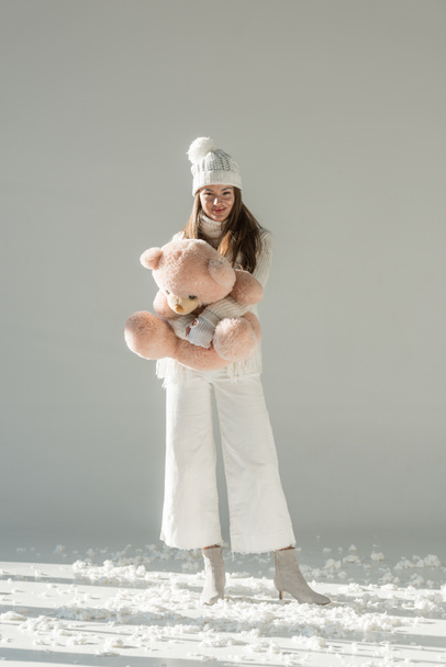 divatos téli pulóver és a gazdaság puha medve játék és látszó-on fényképezőgép-fehér kendő, vonzó nő - Fotó, kép