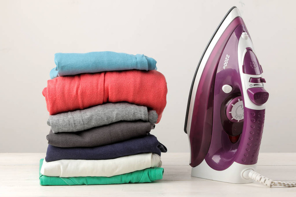 lilac iron and a stack of clothes on a light background. ironing clothes. household electrical appliances. - Photo, Image