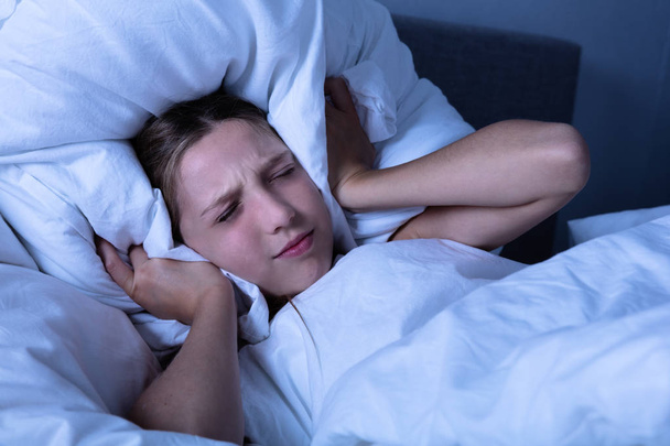 Tyttö häiritsee melua peittää hänen korvansa tyynyllä
 - Valokuva, kuva