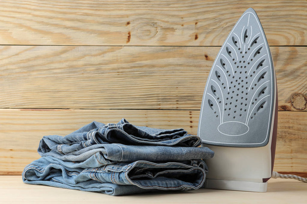 Fliederbügeleisen und ein Stapel Jeans auf einem natürlichen Holzgrund mit Platz für Text. Wäsche bügeln. Elektrische Haushaltsgeräte. - Foto, Bild