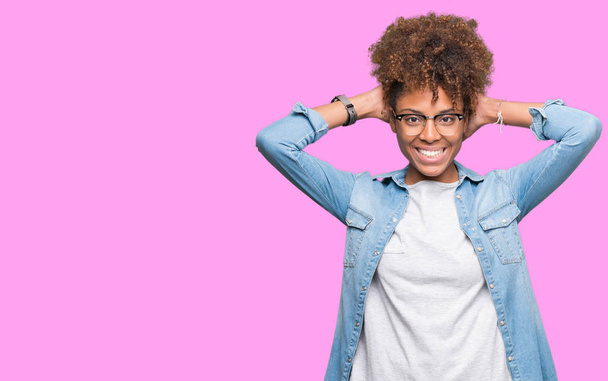 Mooie jonge african american vrouw dragen bril over geïsoleerde achtergrond ontspannend en rekken met armen en handen achter het hoofd en de nek, glimlachend gelukkig - Foto, afbeelding