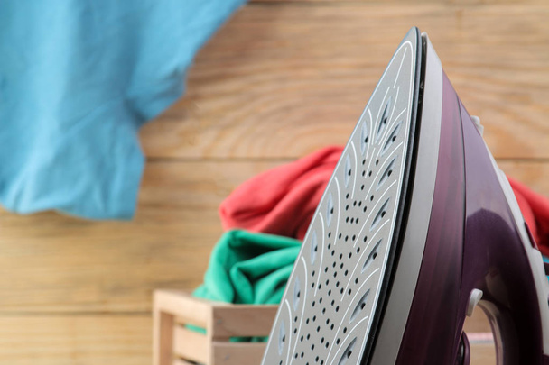 Fliederbügeleisen und ein Stapel Kleidung in einer Schachtel auf einem natürlichen Holzgrund. Wäsche bügeln. Elektrische Haushaltsgeräte. - Foto, Bild