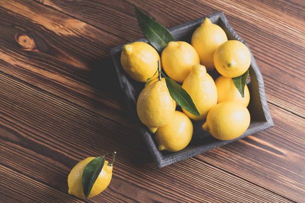 Fresh yellow lemons with leaves lie on a wooden table.  - Фото, изображение