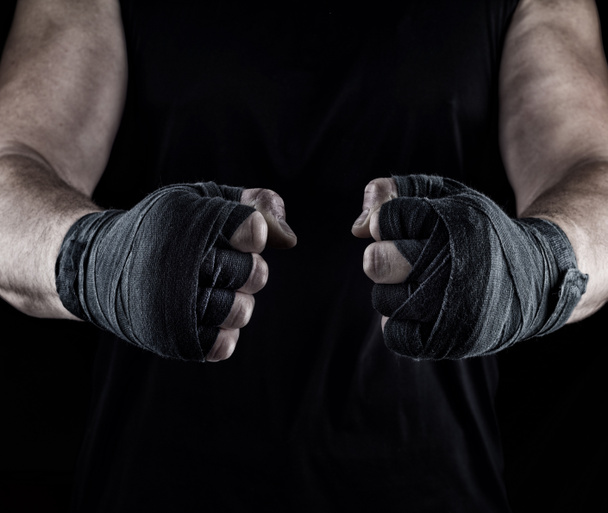  men's hands wrapped in a black bandage, body parts in front of the torso, black background - Photo, Image