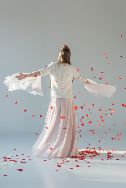 back view of attractive woman in fashionable winter outfit spinning around under falling red roses petals on white - Photo, image