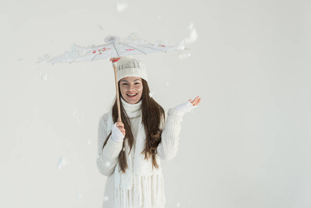 happy attractive woman in fashionable winter sweater and scarf standing under paper umbrella, snow falling isolated on white - Zdjęcie, obraz