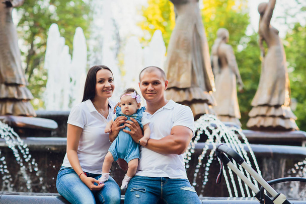manželé sedí na okraji městské fontány, dítě v náručí, pojetí lásky - Fotografie, Obrázek