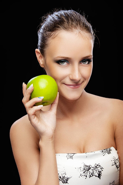 Jonge lachende mooie vrouw met donkere haren met groene appel, geïsoleerd op zwarte achtergrond. - Foto, afbeelding