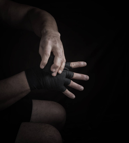 Мужчина заворачивает руки в черную текстильную повязку для спорта, черный фон - Фото, изображение