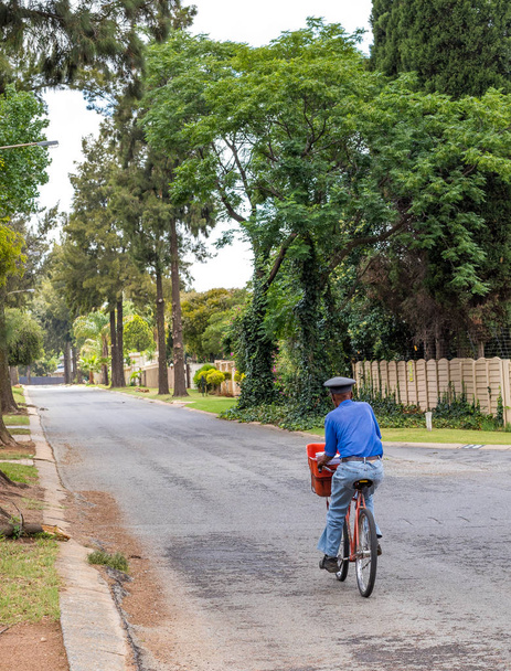 Johannesburg, South Africa - December 10, 2018: an unidentified postman makes hand deliveries on bicycle in a residential suburb in the city image with copy space in portrait format - 写真・画像