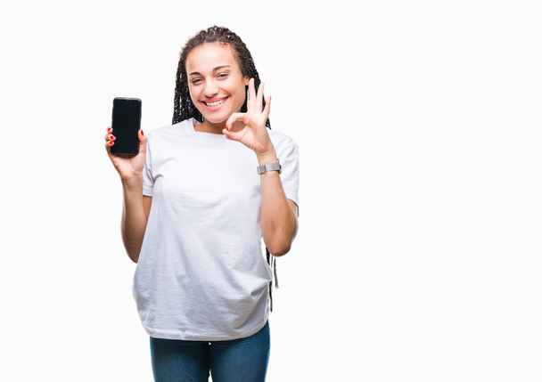 Молода плетене волосся афроамериканська дівчина, що показує екран смартфона на ізольованому фоні, робить знак з пальцями, відмінний символ
 - Фото, зображення