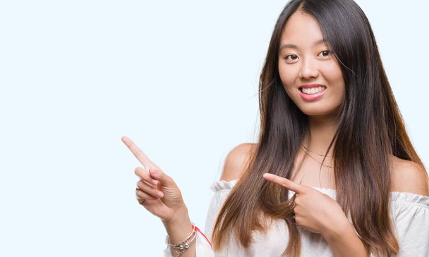 Young asian woman over isolated background smiling and looking at the camera pointing with two hands and fingers to the side. - Foto, Imagen