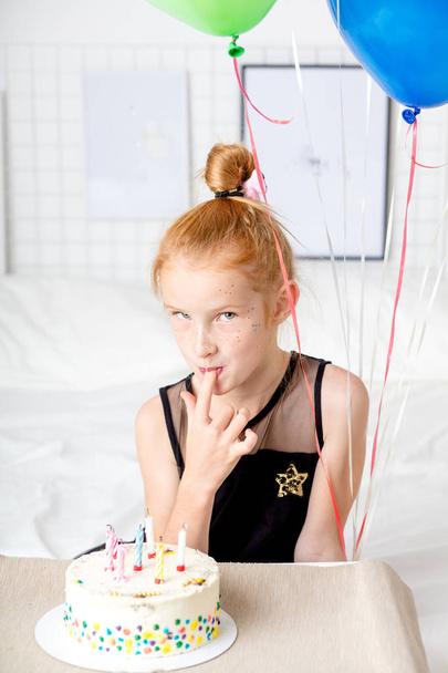 Pretty little ginger girl tasting yummy birthday cake with a finger - Photo, Image