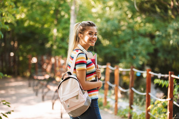 Image of a happy young cute girl student walking in park with backpack. - Foto, immagini