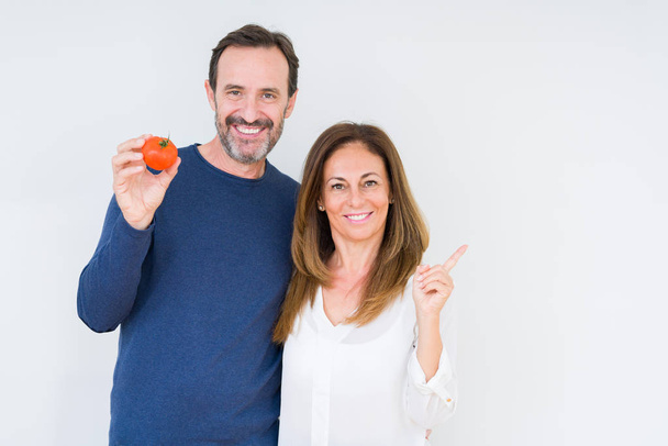 Keski-ikäinen pari syö tuoretta tomaattia yli eristetty tausta erittäin onnellinen osoittaa käsin ja sormella sivulle
 - Valokuva, kuva