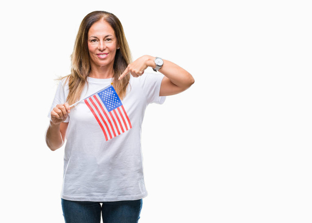 Donna ispanica di mezza età che tiene la bandiera degli Stati Uniti d'America su sfondo isolato con faccia a sorpresa che punta il dito verso se stesso
 - Foto, immagini