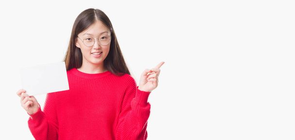 Jonge Chinese vrouw over geïsoleerde achtergrond met lege kaart erg blij met de hand en de vinger te wijzen naar de kant - Foto, afbeelding