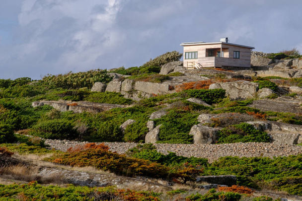 small wooden house at the top of cliffs with bushes and stones in the foreground - Fotografie, Obrázek