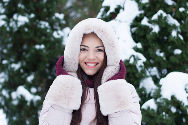 Портрет молодої красивої емоційної жінки з капюшоном і рукавичками на засніженому садовому тлі. Зимовий сніжний пейзаж
 - Фото, зображення
