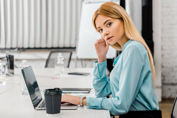 вид збоку привабливої бізнес-леді на робочому місці з ноутбуком і кавою, щоб піти в офіс
 - Фото, зображення