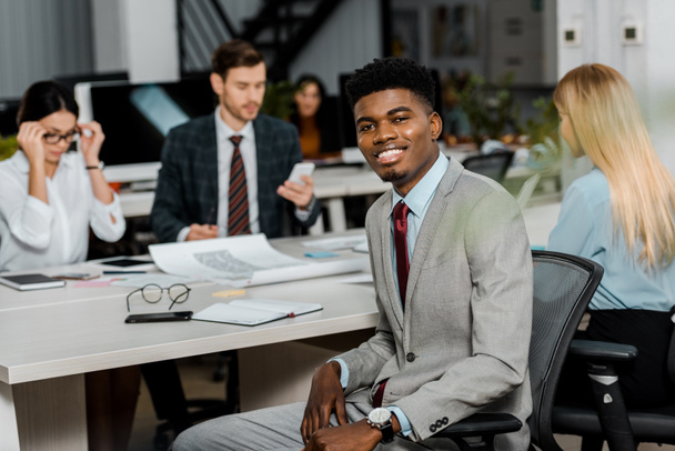 enfoque selectivo de sonriente hombre de negocios afroamericano y colegas de negocios en el lugar de trabajo en la oficina
 - Foto, imagen