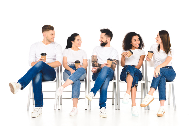 multicultural group of people sitting on chairs with coffee to go and speaking isolated on white - Foto, Imagem