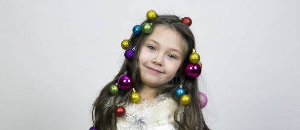 Girl with Christmas decorations in her hair. Little beautiful girl braided Christmas tree decorations in her hair. - Photo, Image