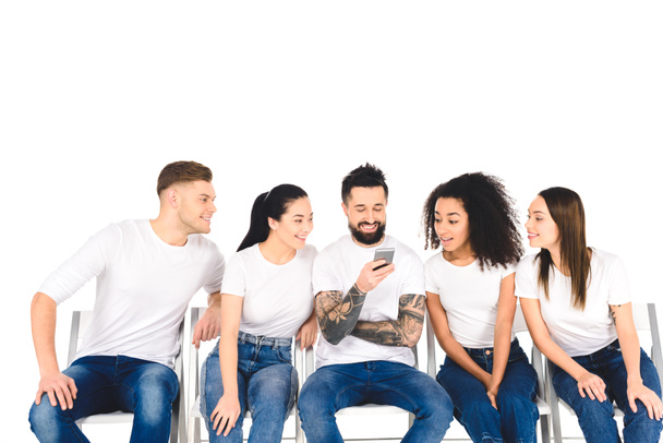 smiling tattooed man using smartphone while multiethnic curious young people looking at screen isolated on white - Fotoğraf, Görsel