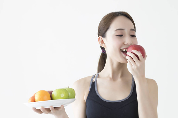 Young Asian woman wearing a dress holding a plate of fruits and smiling eating an apple - Foto, Bild