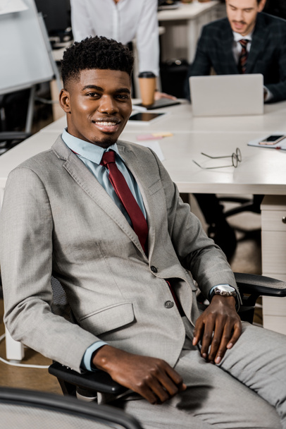 smiling african american businessman looking at camera at workplace in office - Фото, изображение