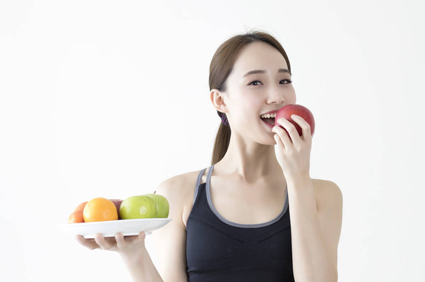 Young Asian woman wearing a dress holding a plate of fruits and smiling eating an apple - Foto, Imagem