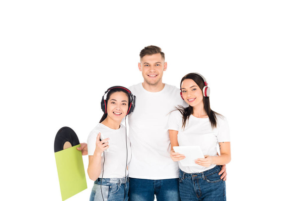 jovens em fones de ouvido abraçando e segurando disco de vinil e tablet digital isolado em branco
 - Foto, Imagem