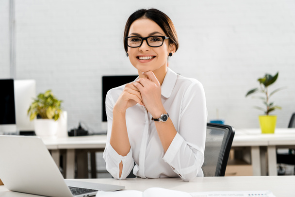 ritratto di donna d'affari sorridente in occhiali a posto di lavoro con computer portatile in ufficio
 - Foto, immagini