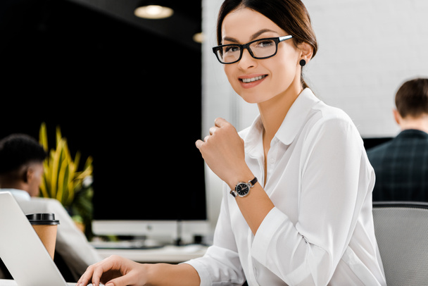 smiling businesswoman in eyeglasses at workplace with laptop in office - Φωτογραφία, εικόνα