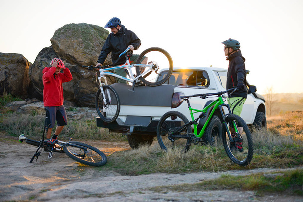 Friends Taking MTB Bikes off the Pickup Offroad Truck in Mountains at Sunset. Adventure and Travel Concept. - Foto, imagen