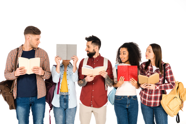 multicultural group of people holding backpacks and looking at girl with book isolated on white - Photo, Image