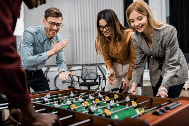 smiling multicultural business colleagues playing table football together in office - Fotó, kép